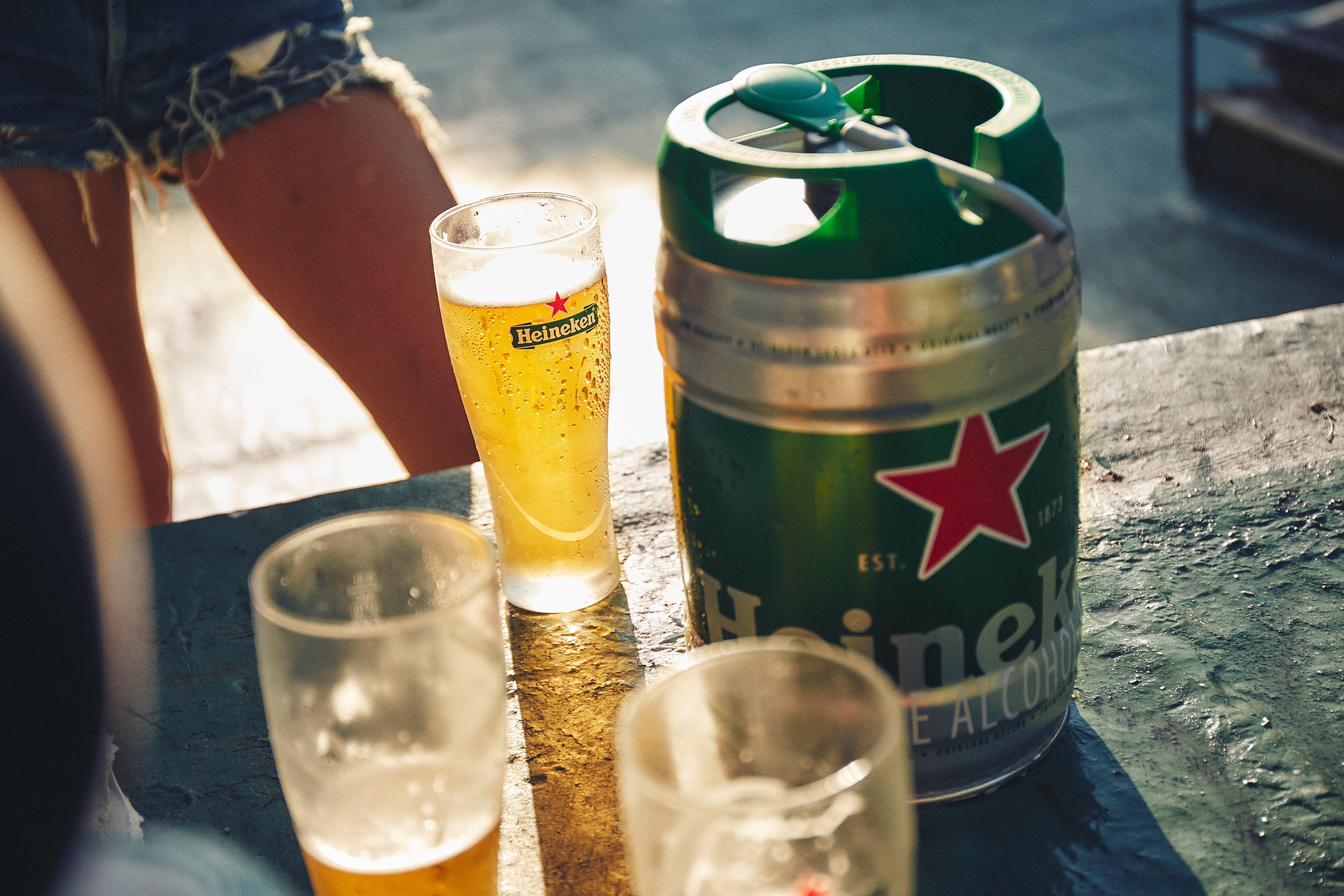 A 5L keg of Heineken beer is shared among friends in a sunny, outdoor setting, highlighting a moment of leisure and refreshment.