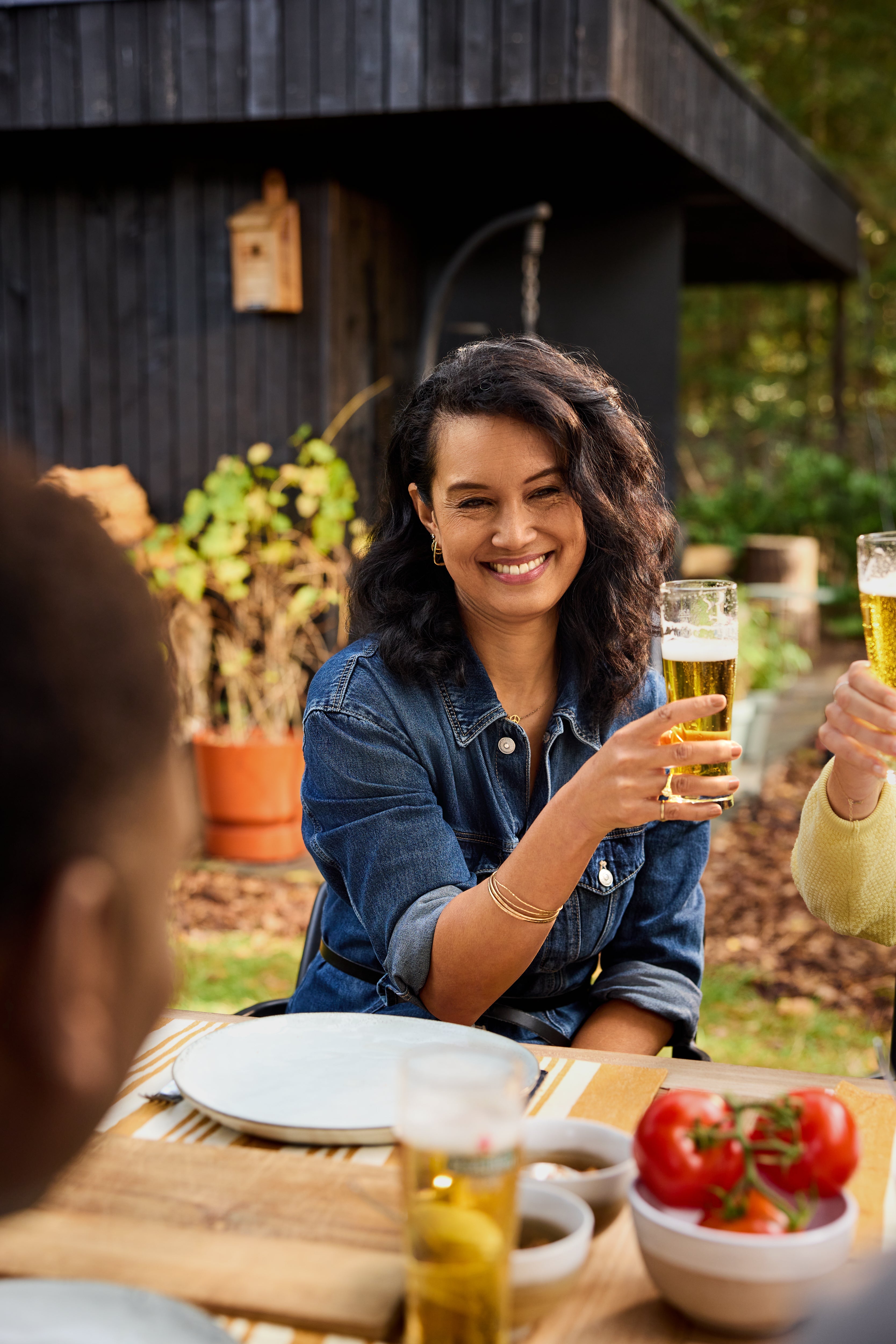 Woman sitting at a table outdoors, holding a glass of beer with another person.