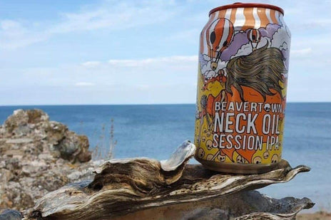 A can of Beavertown Neck Oil session IPA rested on a rock with the sea in the background.