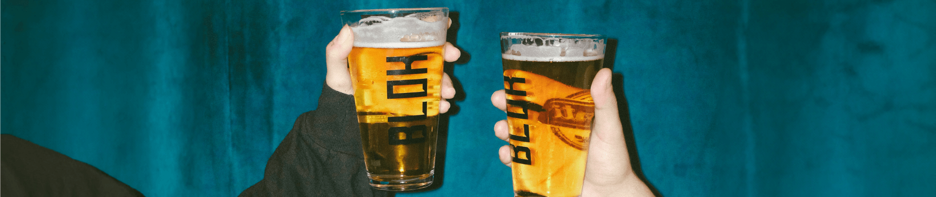 Two hands holding up pint glasses filled with lager against a deep blue background.