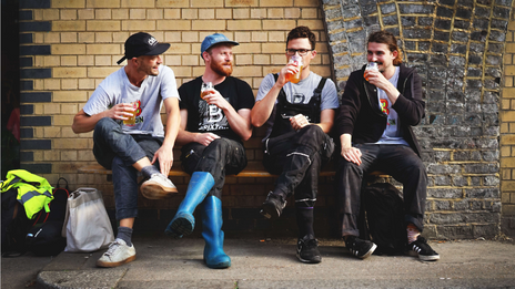 A group of four brewers from the Brixton brewery enjoying a beer together on a bench.