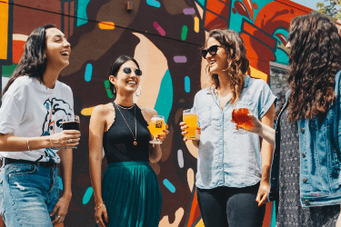 A group of friends enjoying beer outside next to a colourful wall.