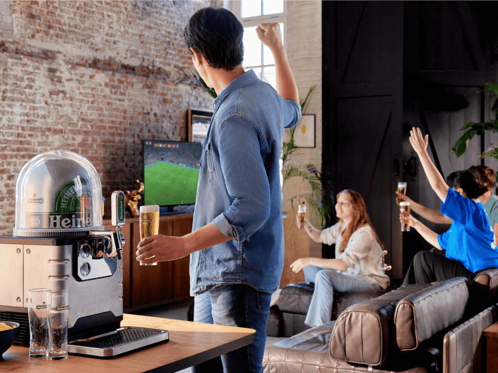 A group of friends watching sports on TV at home and drinking Heineken beer from a BLADE beer machine.