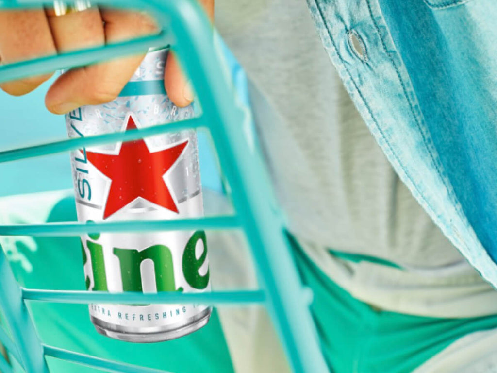 A person wearing a blue shirt holds a can of ice cold Heineken Silver beer.