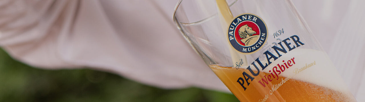 A bottle of beer being poured into a Paulaner Weissbier glass.